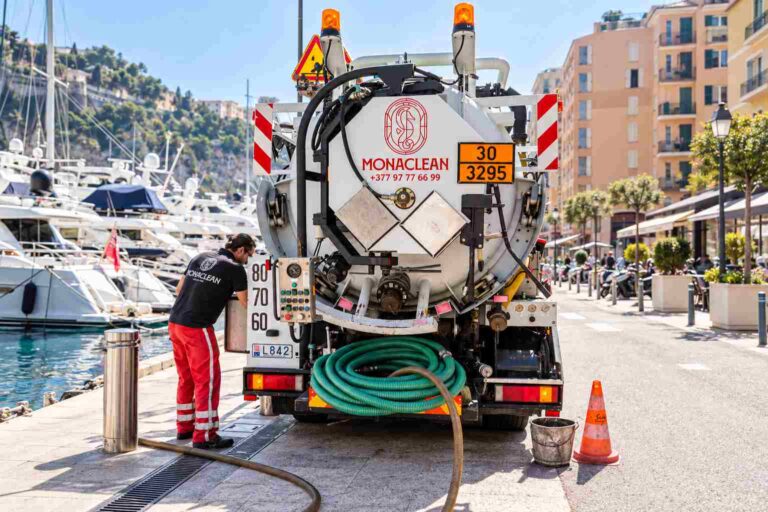 Technicien Monaclean intervenant à l’arrière d’un camion d’assainissement stationné sur un quai, à proximité de yachts.